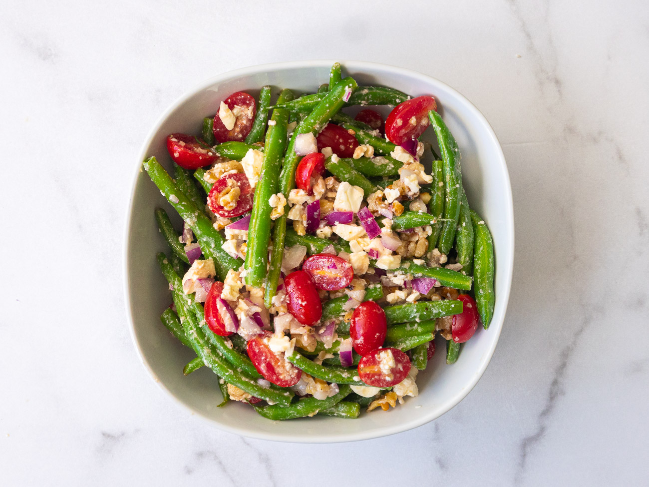 Top down photo of green beans, feta cheese, tomatoes, and walnuts in a bowl
