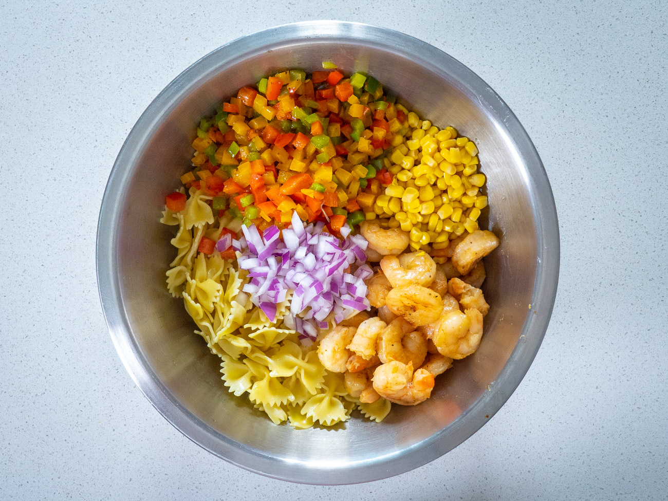Ingredients for pasta salad in a large metal bowl